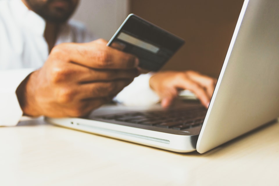 A hand holding a card while typing on a laptop to complete an online payment