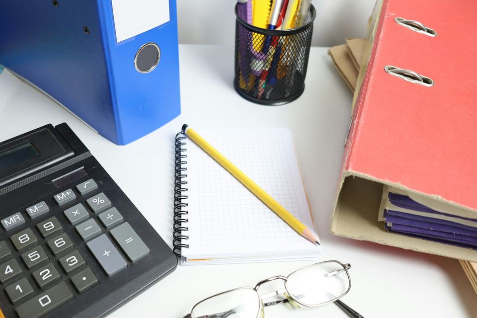 A calculator, binders and a notebook on a desk, set up for doing invoicing paperwork