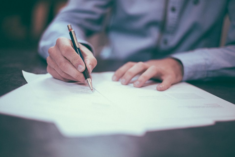 A hand filling in paperwork on a desk, representing digital record keeping for tax