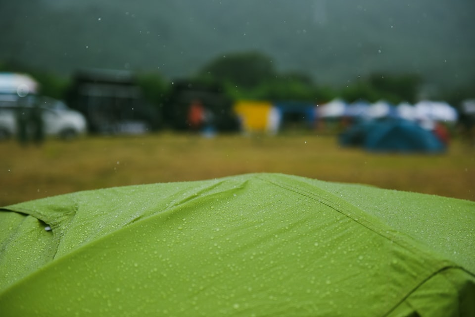 Raindrops on a green tent with other tents and vehicles in the misty background at a UK campsite