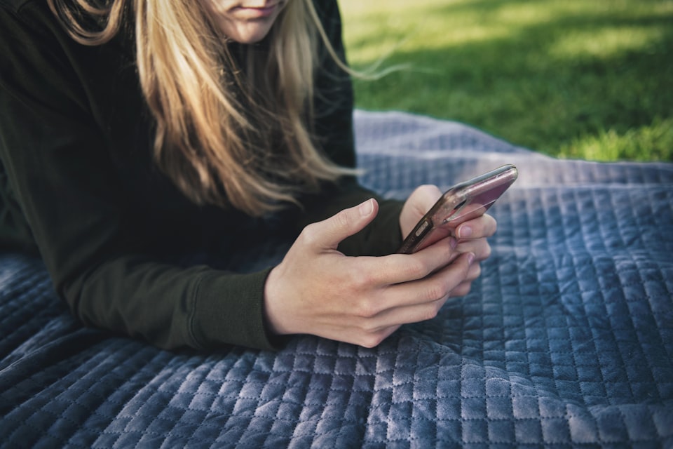 A person sitting outside on a picnic blanket reading something on their phone