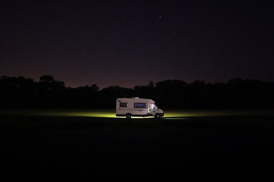 A motorhome lit up at night parked alone in a dark campsite field