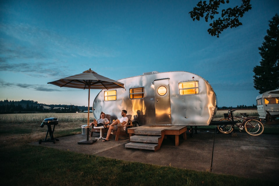 A touring caravan on a pitch at dusk with a couple relaxing outside