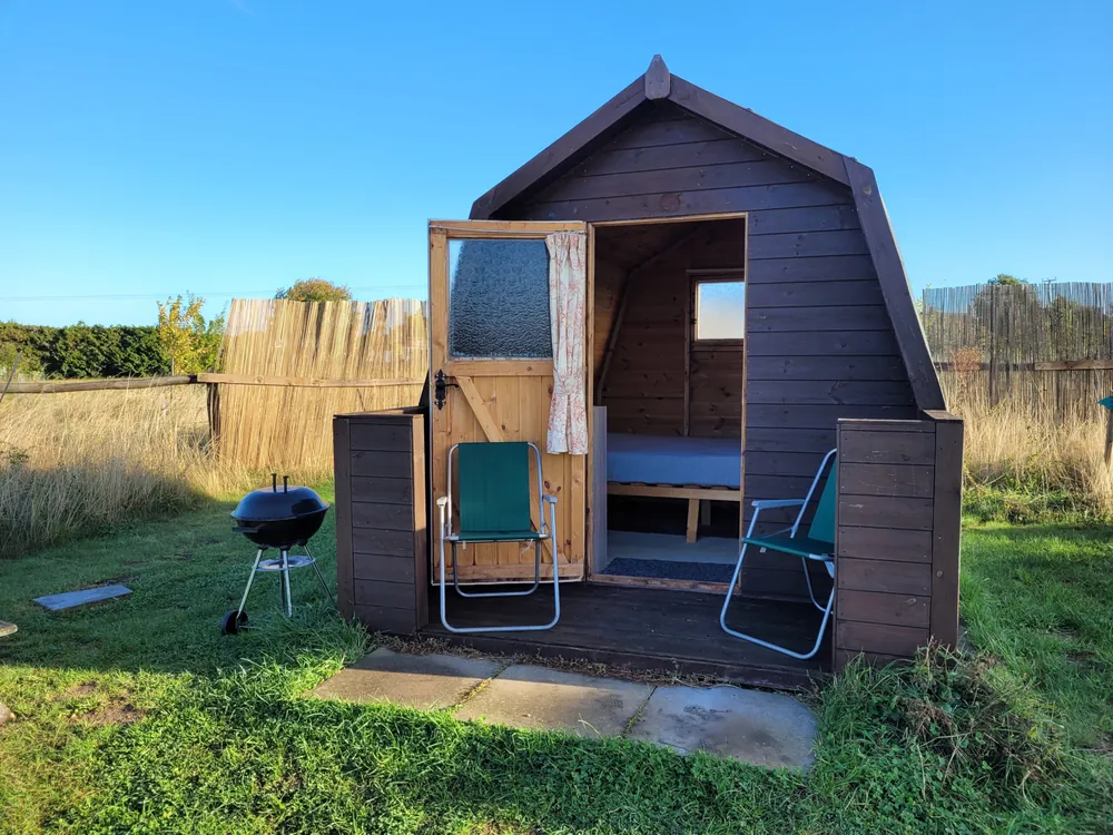 A wooden log pod at Bredon-Vale with two camping chairs and a barbecue outside