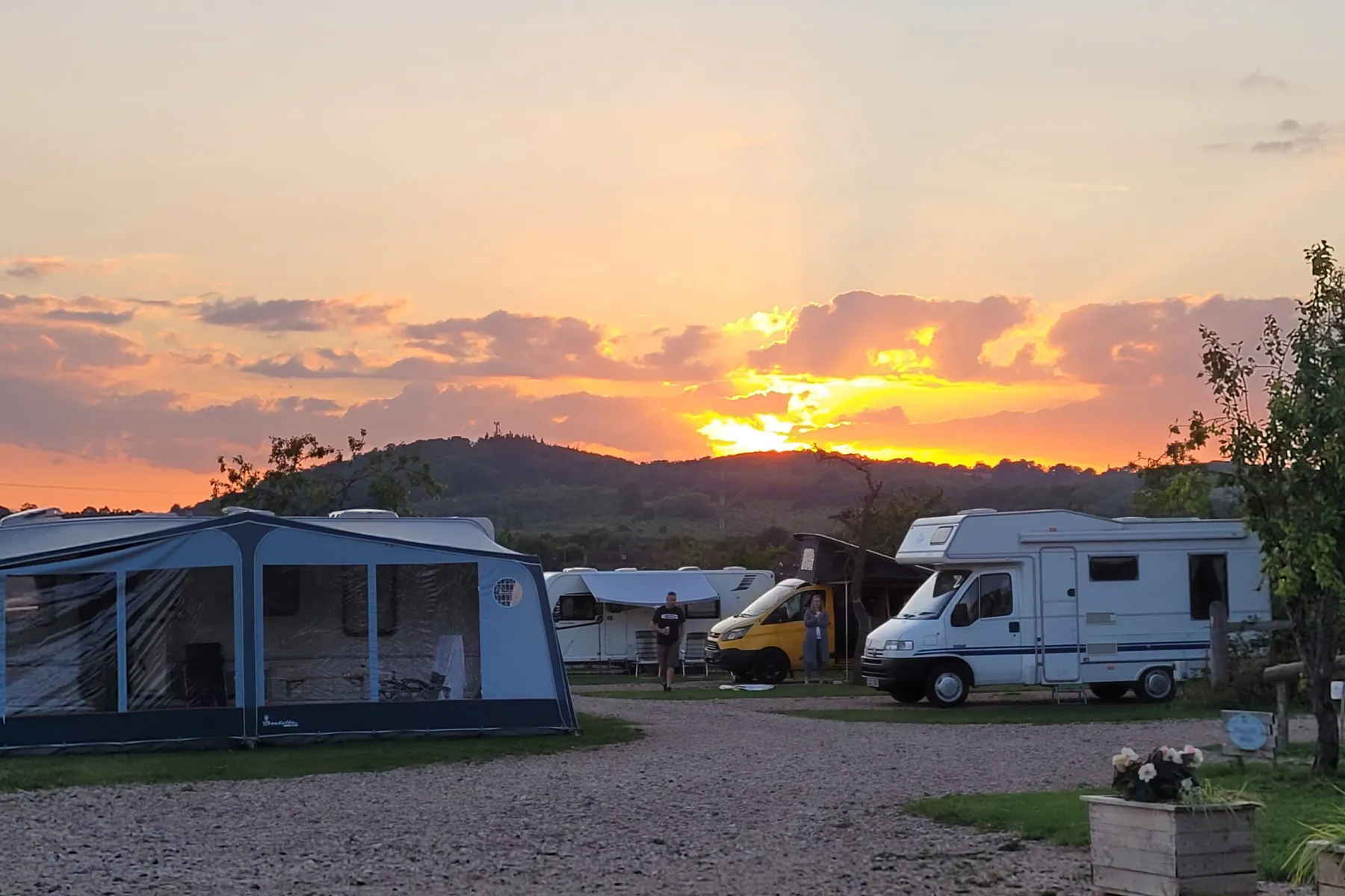 Caravans and motorhomes on the hardstanding pitches at Bredon-Vale with the sun setting behind Bredon Hill